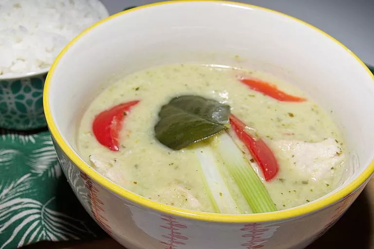 A traditional bowl of creamy, aromatic Thai green curry with chunks of chicken in a small bowl with jasmine rice